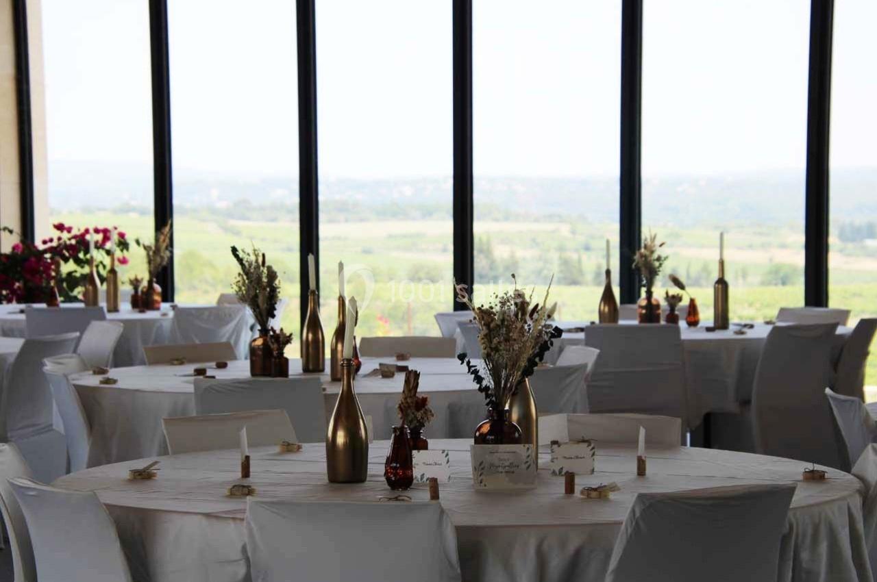 Salle de réception lumineuse avec tables rondes décorées de nappes blanches et centres de table floraux.