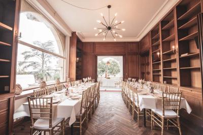Salle lumineuse décorée pour un événement, avec des tables dressées, des chaises dorées et des fleurs en centre de table.