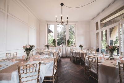 Salle lumineuse décorée pour un événement, avec des tables dressées, des chaises dorées et des fleurs en centre de table.