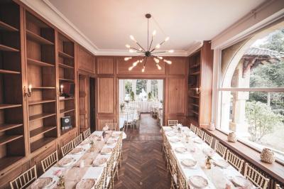 Salle lumineuse décorée pour un événement, avec des tables dressées, des chaises dorées et des fleurs en centre de table.