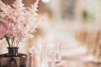Salle lumineuse décorée pour un événement, avec des tables dressées, des chaises dorées et des fleurs en centre de table.