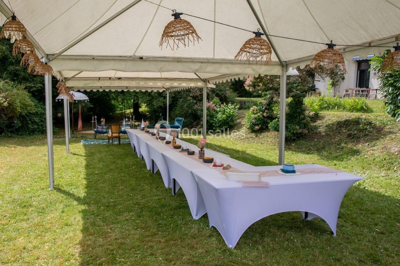 Tables rectangulaires décorées sous une tente blanche dans un jardin verdoyant.