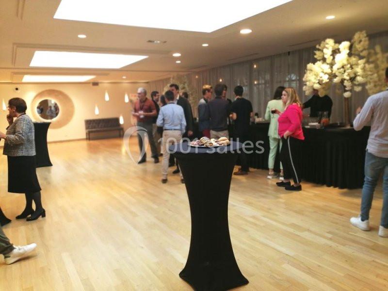 Personnes discutant dans une salle lumineuse avec un buffet et une table haute garnie de petits gâteaux au premier plan.