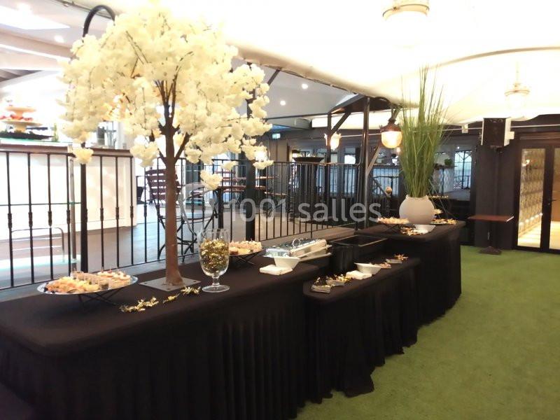 Table de buffet avec nappes noires, décorée d'un arbre artificiel fleuri et de plats disposés dans un espace intérieur…