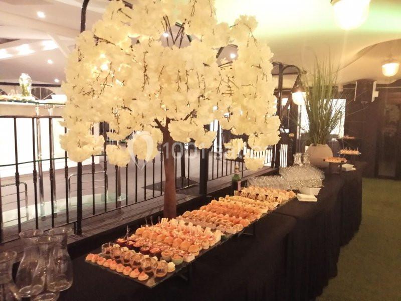 Table de buffet garnie de verrines et amuse-bouches, décorée avec un arbre artificiel aux fleurs blanches.