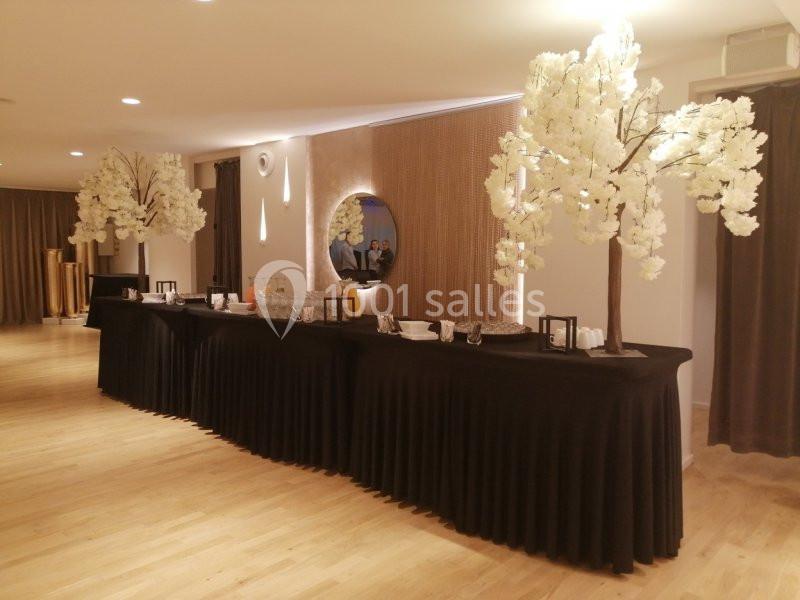 Table de réception décorée de nappes noires, ornée de vaisselle et de deux arbres artificiels blancs dans une salle…