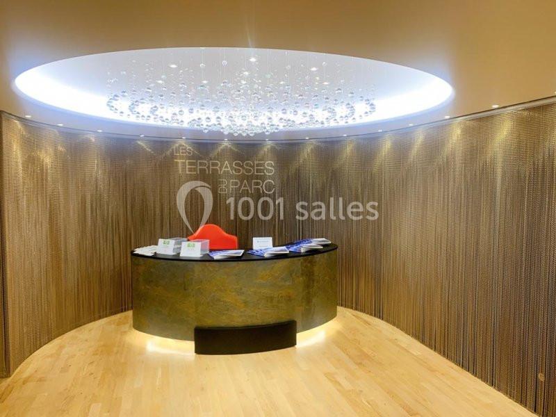 Accueil avec un comptoir arrondi, une chaise rouge, des brochures et un mur décoratif en métal perforé.