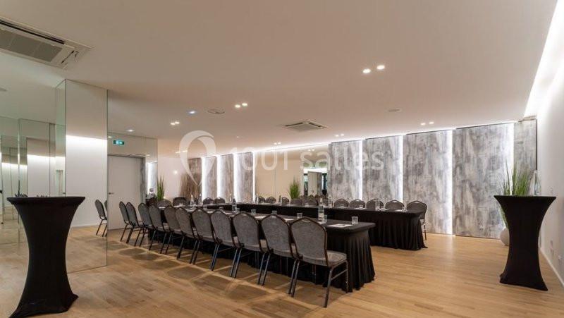 Salle de réunion lumineuse avec une grande table rectangulaire entourée de chaises, parquet clair et murs modernes.