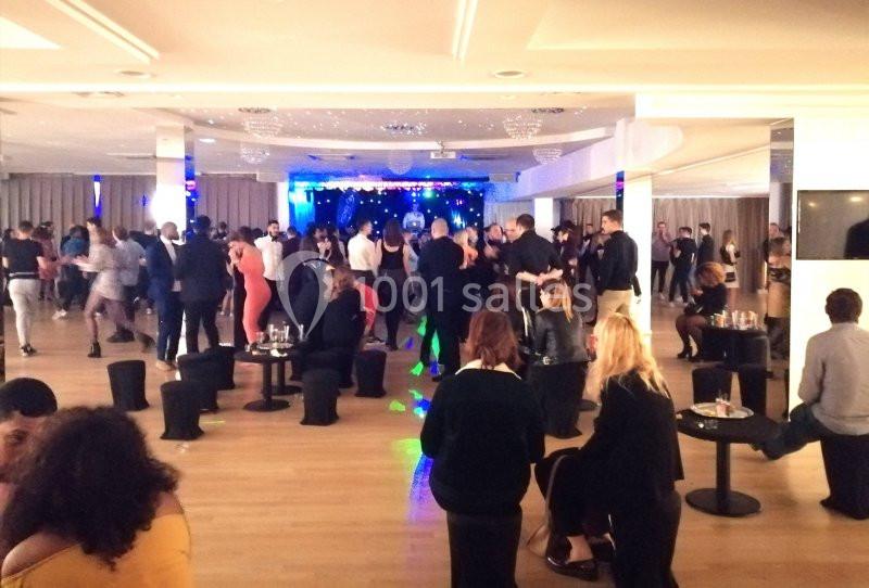 Personnes dansant et discutant dans une grande salle éclairée, avec des tables et des chaises disposées autour.