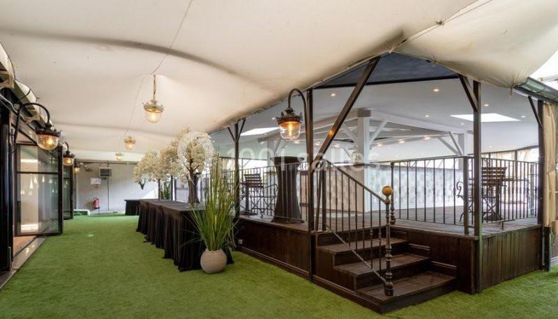 Espace intérieur lumineux avec sol en gazon synthétique, estrade en bois, tables et décorations florales blanches.