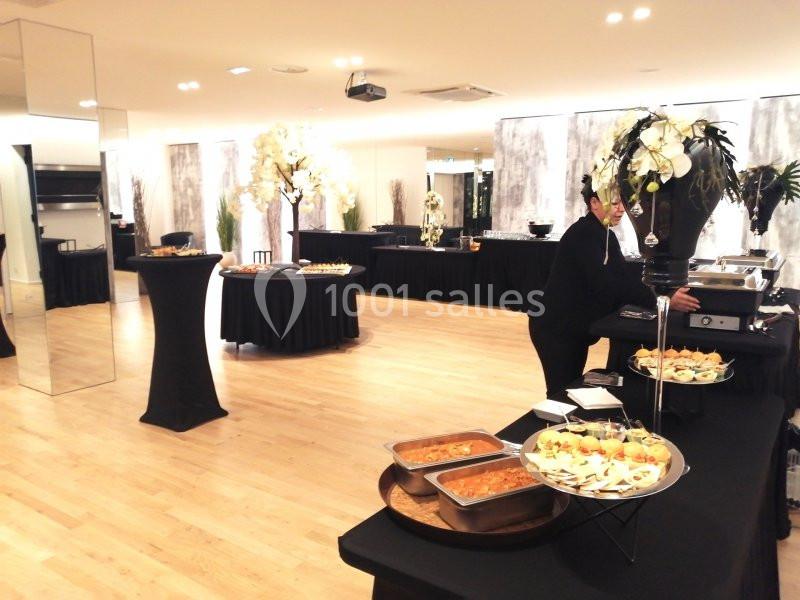 Salle de réception lumineuse avec buffet disposé sur des tables noires et serveuse en action.