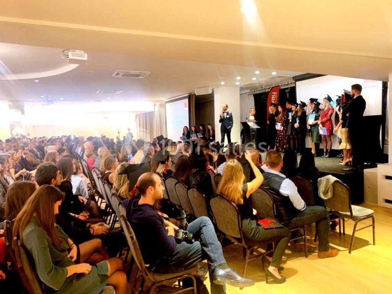 Cérémonie de remise de diplômes avec des étudiants sur scène et un public assis dans une salle éclairée.
