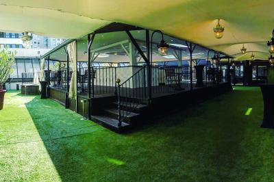 Terrasse extérieure avec pelouse artificielle, pergola couverte et immeubles en arrière-plan par temps ensoleillé.