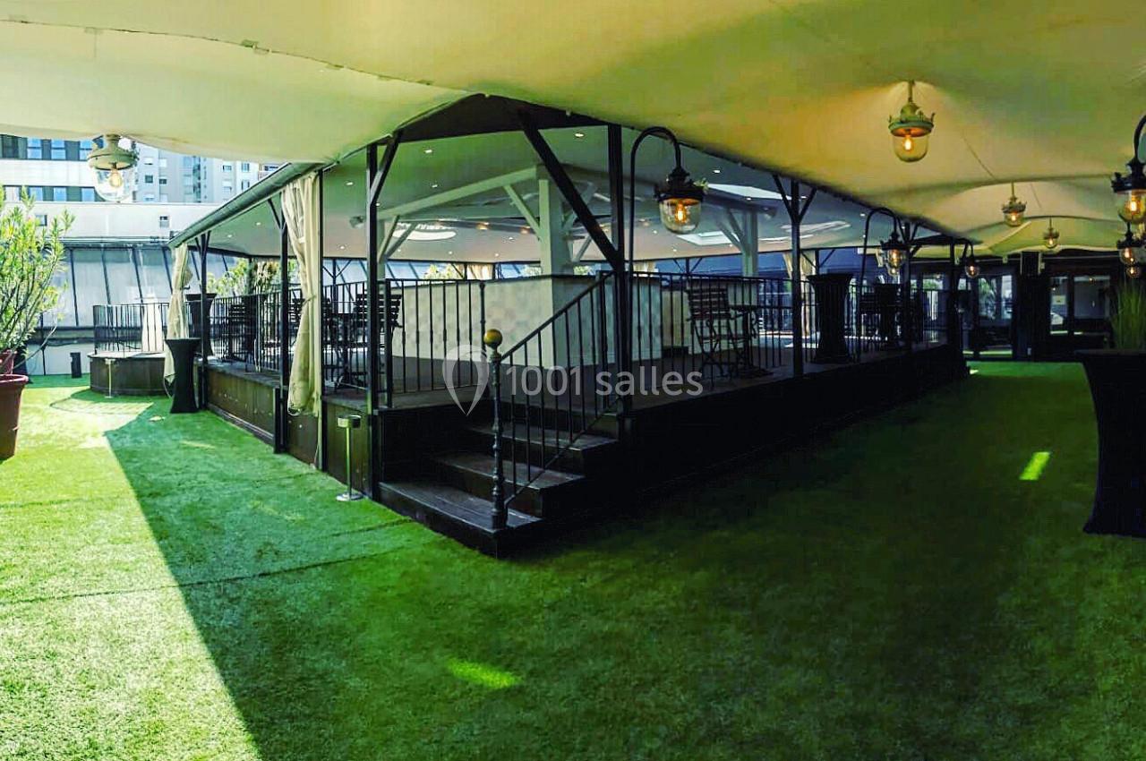 Espace extérieur couvert avec pelouse artificielle, terrasse surélevée et lampes suspendues.