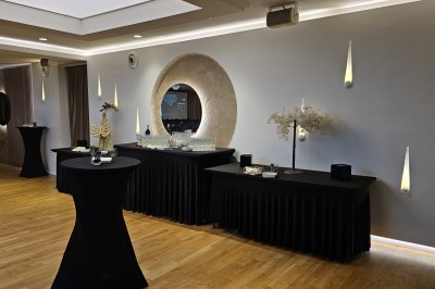 Salle de conférence avec des rangées de chaises noires alignées face à une scène et un écran de projection.