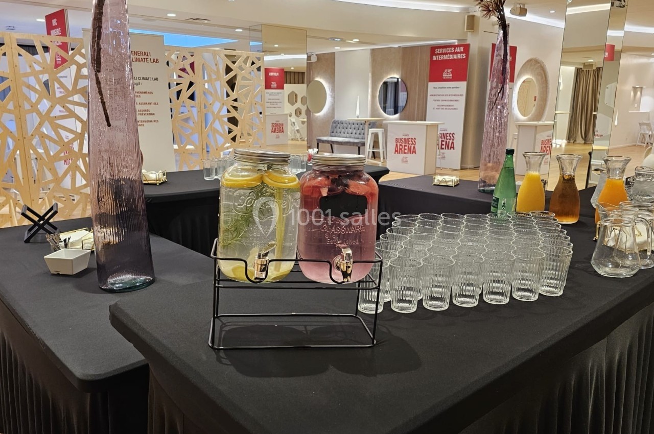 Table avec boissons en libre-service, incluant des carafes d'eau aromatisée, jus, verres et accessoires sur nappe noire.