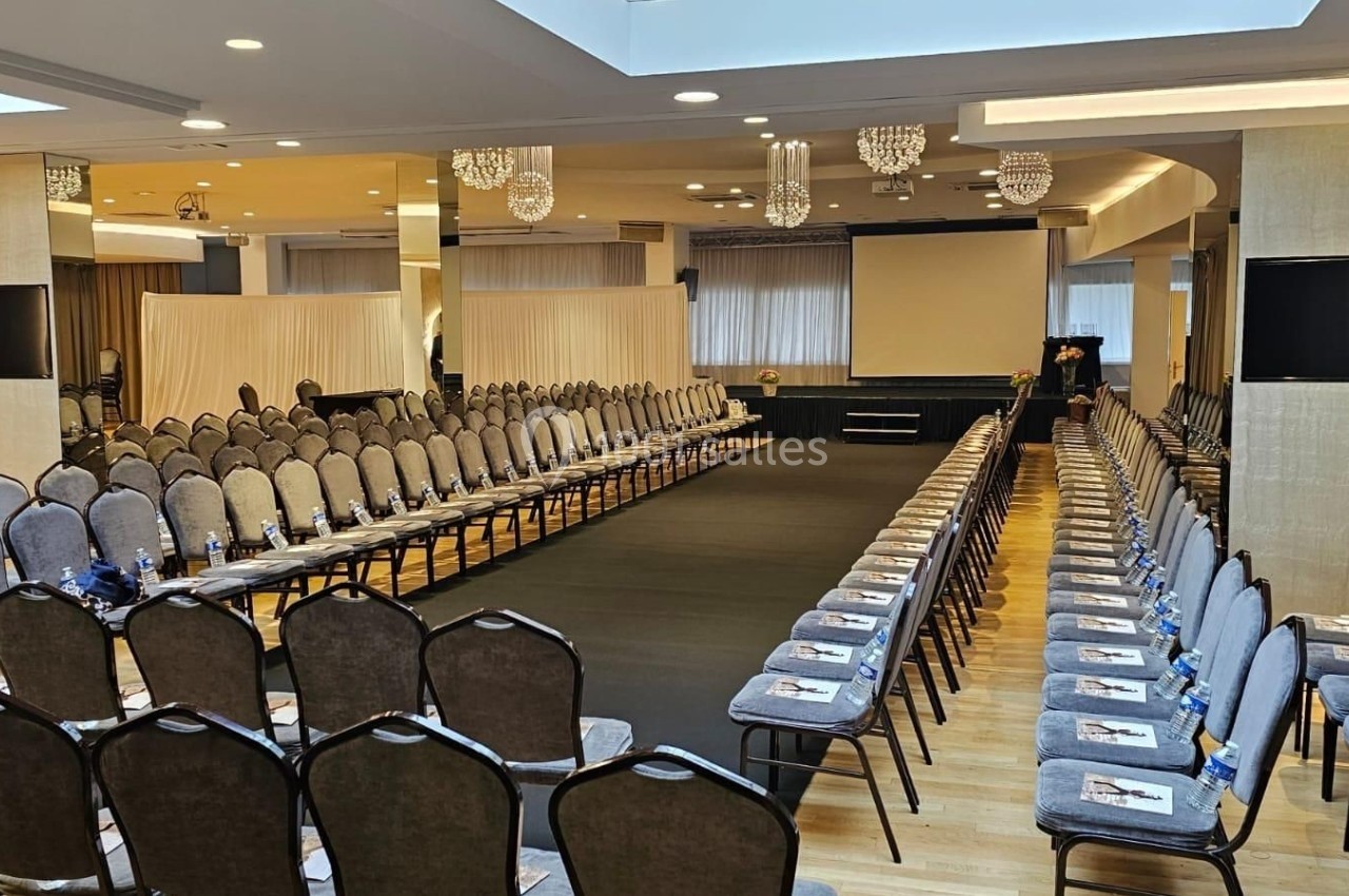 Salle de conférence aménagée avec une scène centrale et des rangées de chaises alignées de chaque côté.
