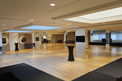 Salle de conférence avec des rangées de chaises noires alignées face à une scène et un écran de projection.