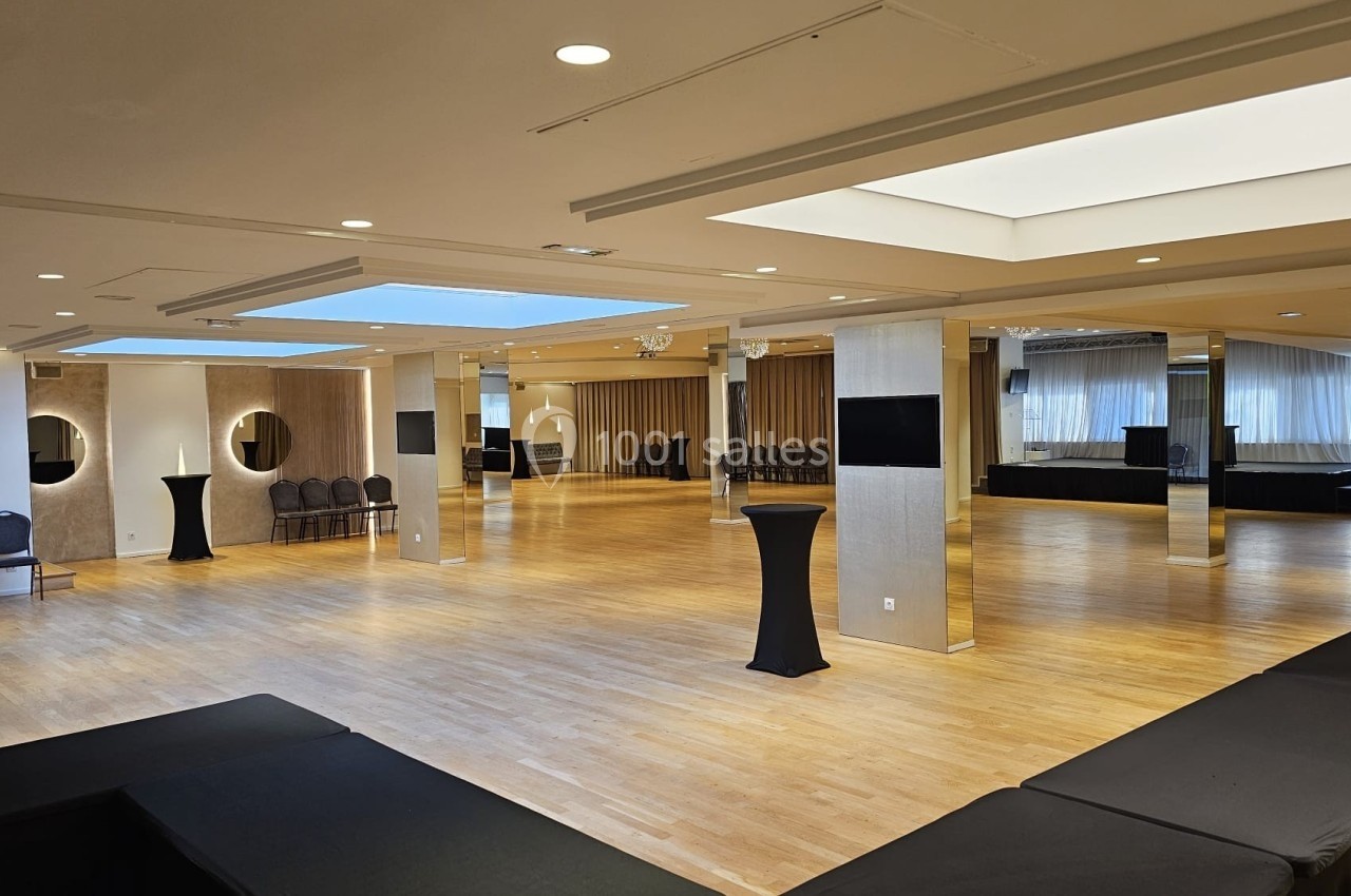 Salle spacieuse avec parquet clair, tables hautes noires, miroirs ronds et grandes baies vitrées laissant entrer la lumière.