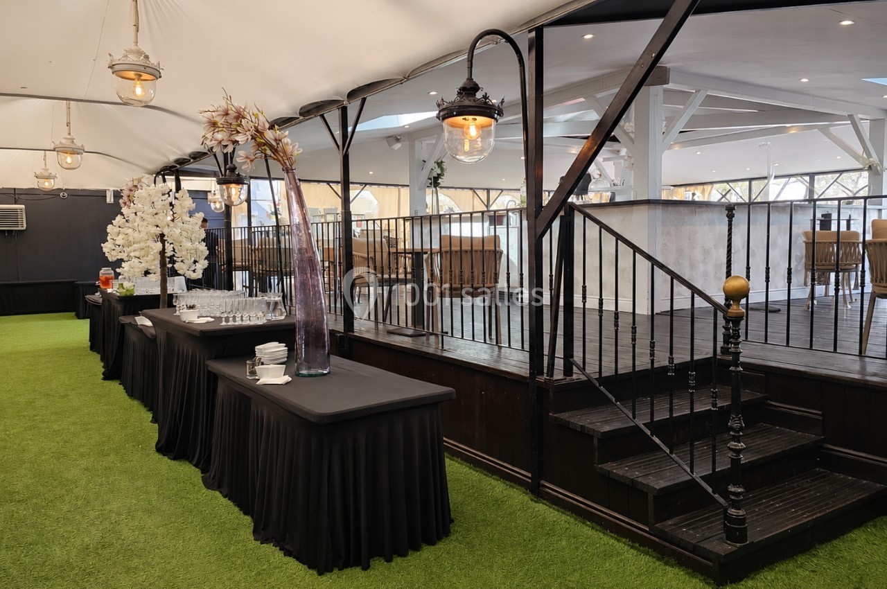 Salle événementielle avec tables drapées de noir, décor floral, escalier en bois et sol recouvert de gazon synthétique.