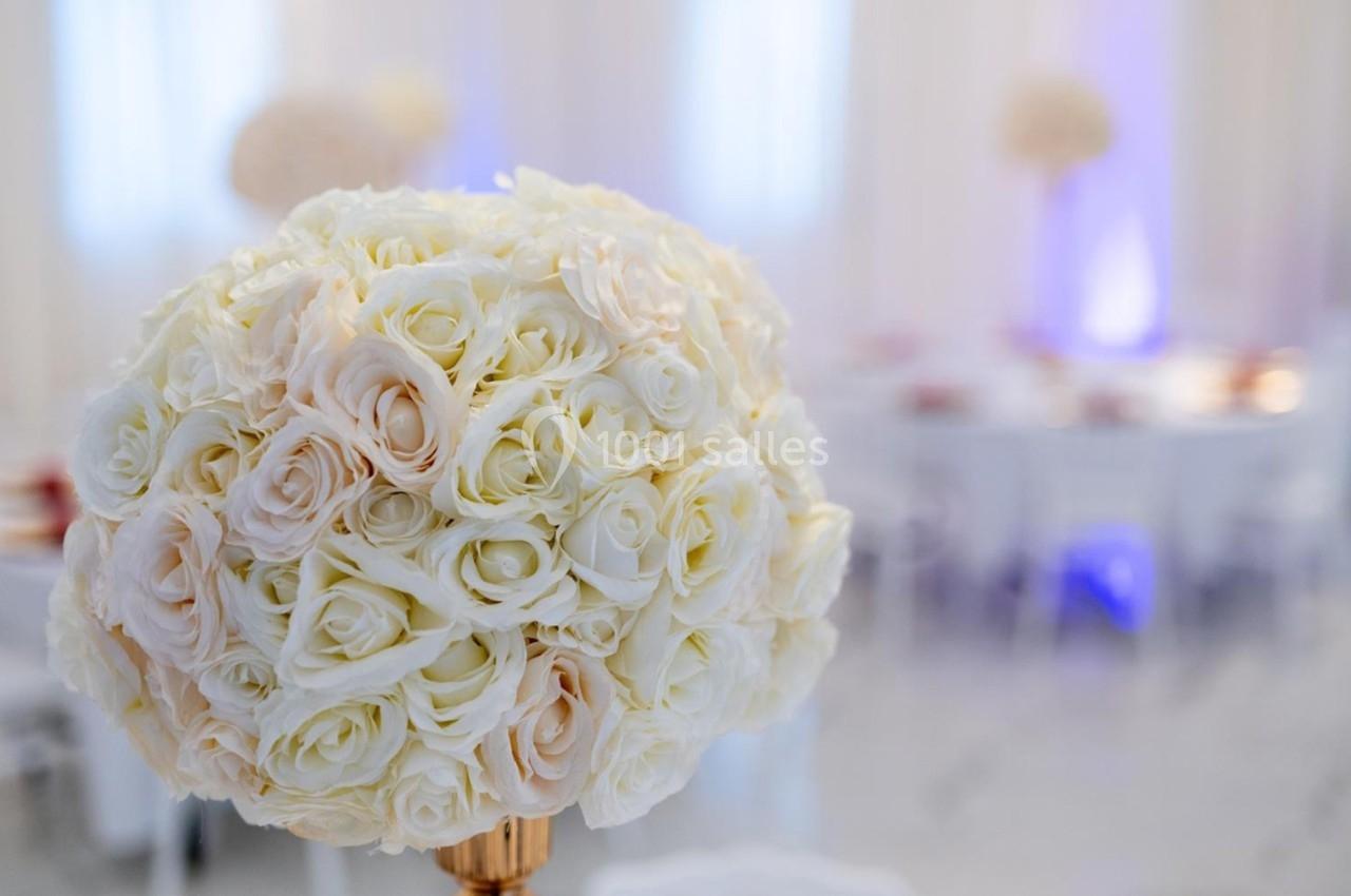 Bouquet rond de roses blanches et crème en gros plan, avec en arrière-plan une salle de réception floutée.