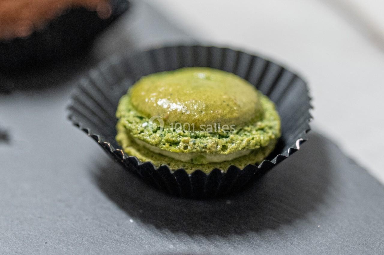 Macaron vert posé dans une caissette noire sur une surface sombre.