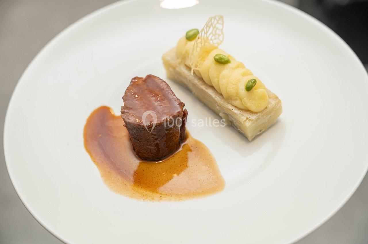 Assiette gastronomique avec un morceau de viande nappé de sauce et un accompagnement de purée sur une base croustillante.