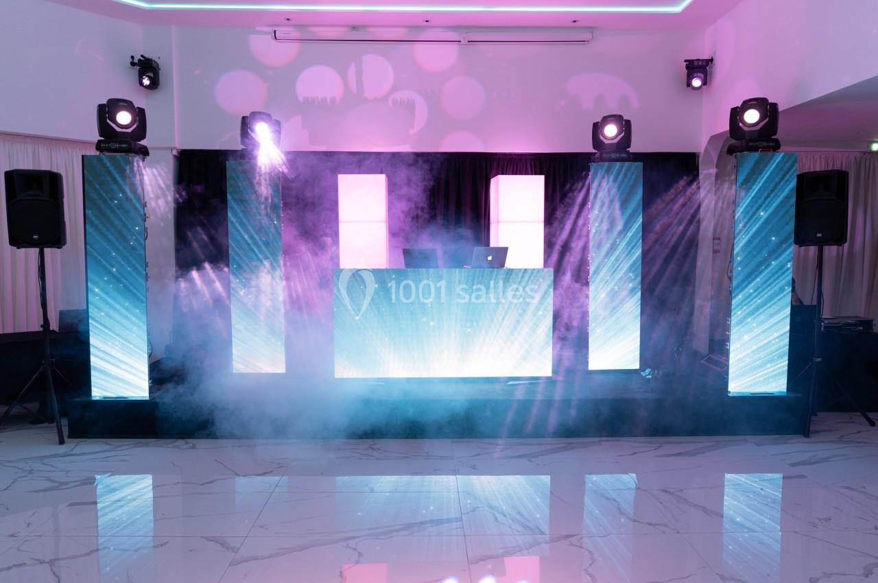 Scène de DJ avec écrans lumineux, projecteurs et fumée dans une salle moderne au sol en marbre.