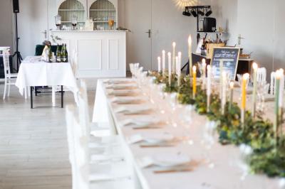 Table élégamment dressée avec nappes blanches, verres, couverts, bouquets de fleurs et petits pots décoratifs.