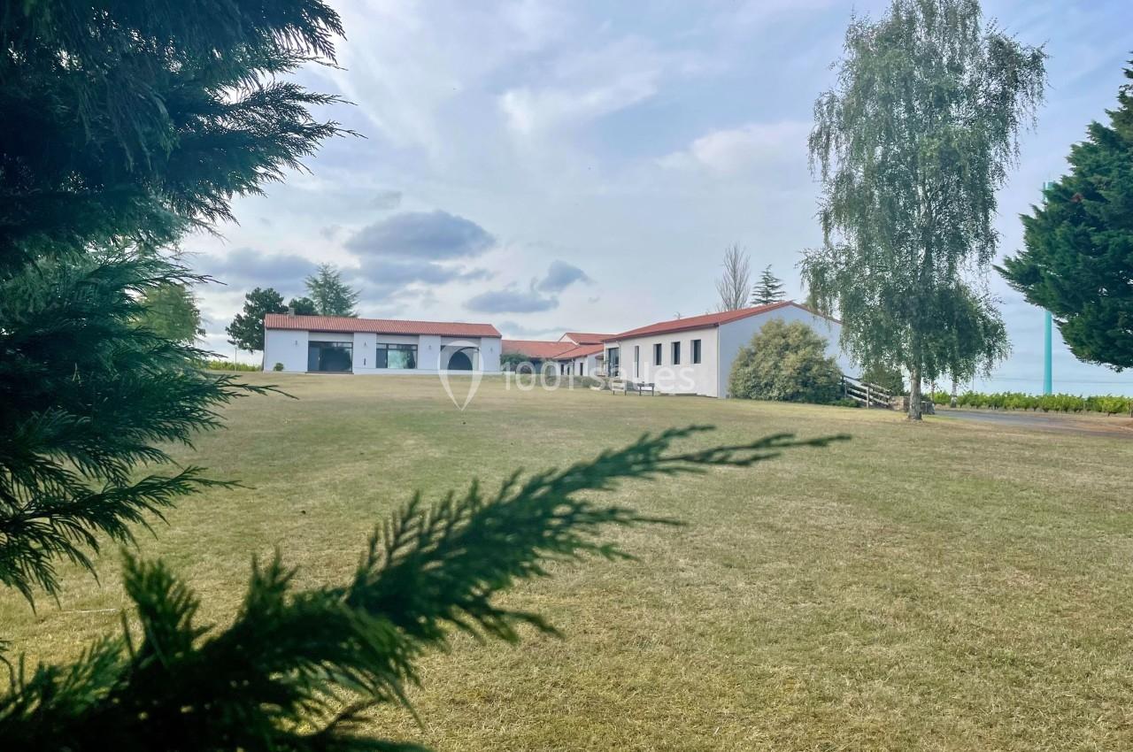 Bâtiment blanc avec toit rouge entouré d'arbres, situé sur une pelouse dégagée sous un ciel partiellement nuageux.