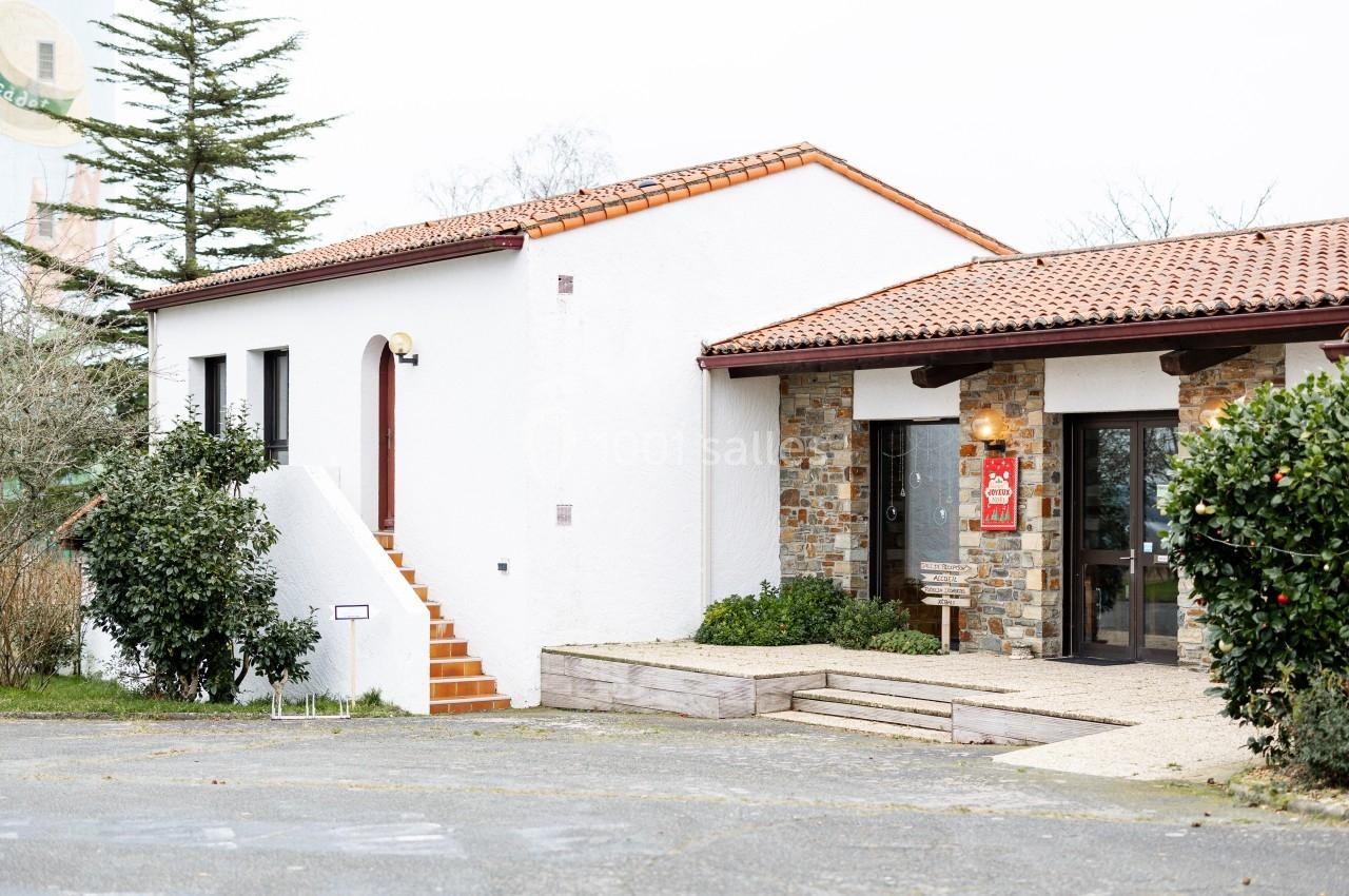 Bâtiment à toit en tuiles rouges avec façade blanche et mur en pierre, entouré de végétation.