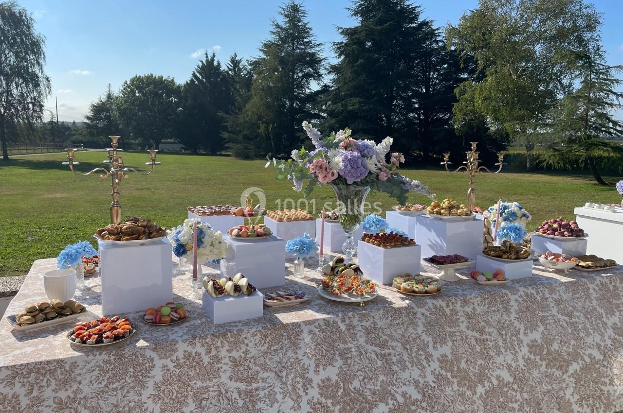 Table décorée en extérieur avec un buffet de desserts variés, fleurs fraîches et chandeliers dorés.