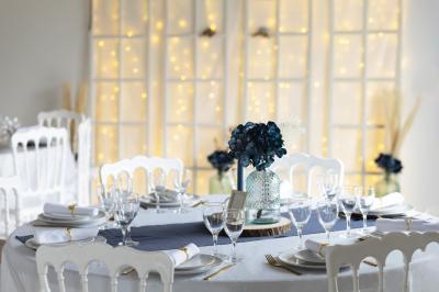 Table élégamment dressée avec nappes blanches, verres, couverts, bouquets de fleurs et petits pots décoratifs.
