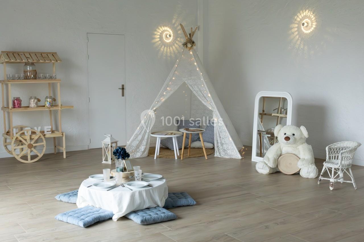 Espace intérieur décoré avec une tente en tissu, un ours en peluche, des coussins et des éléments en bois.