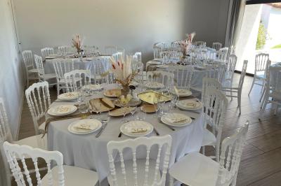 Table élégamment dressée avec nappes blanches, verres, couverts, bouquets de fleurs et petits pots décoratifs.