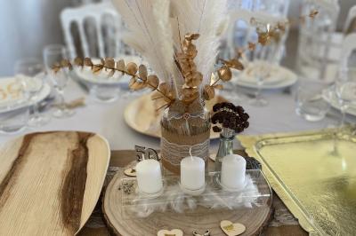 Table élégamment dressée avec nappes blanches, verres, couverts, bouquets de fleurs et petits pots décoratifs.