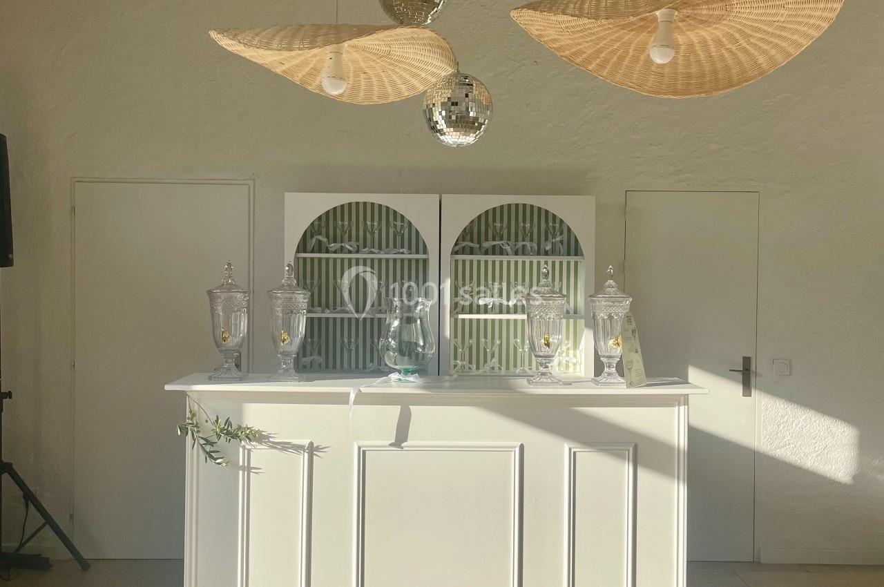 Comptoir blanc décoré avec des lampes suspendues en osier, des boules miroirs et des accessoires en verre dans une pièce…