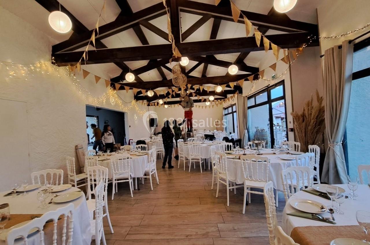 Salle décorée pour un événement, avec tables dressées, guirlandes lumineuses et fanions suspendus au plafond.