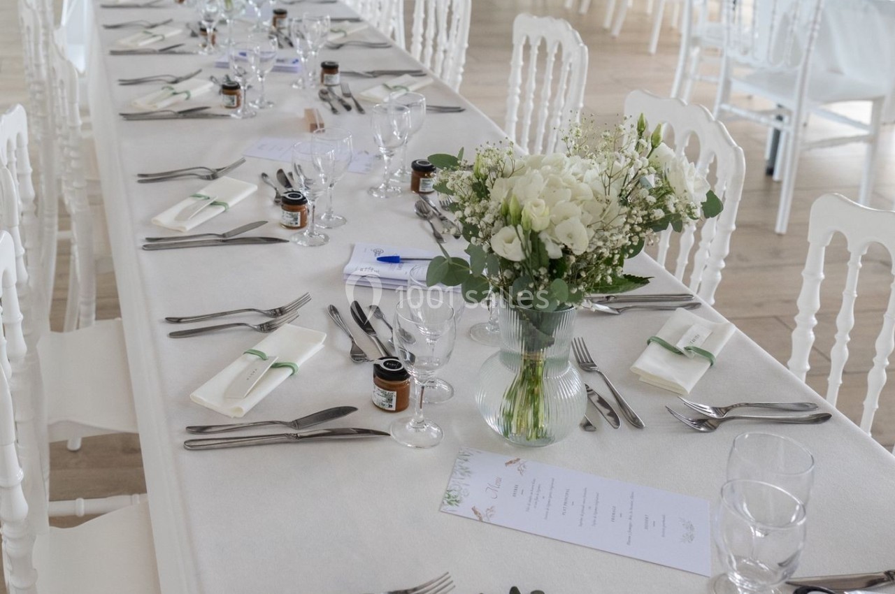 Tables de réception élégamment dressées avec nappes blanches, fleurs, couverts et petits pots en décoration.