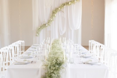 Table élégamment dressée avec nappes blanches, assiettes, verres, serviettes ornées de fleurs et centre de table floral.