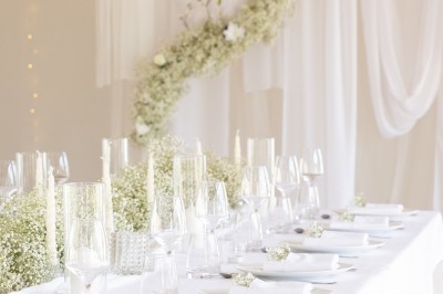 Table élégamment dressée avec nappes blanches, assiettes, verres, serviettes ornées de fleurs et centre de table floral.