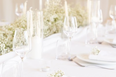 Table élégamment dressée avec nappes blanches, assiettes, verres, serviettes ornées de fleurs et centre de table floral.
