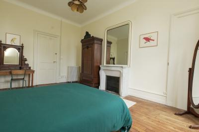 Canapé en velours brun devant une grande fenêtre lumineuse, entouré de rideaux beiges et de meubles en bois.