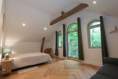 Canapé en velours brun devant une grande fenêtre lumineuse, entouré de rideaux beiges et de meubles en bois.