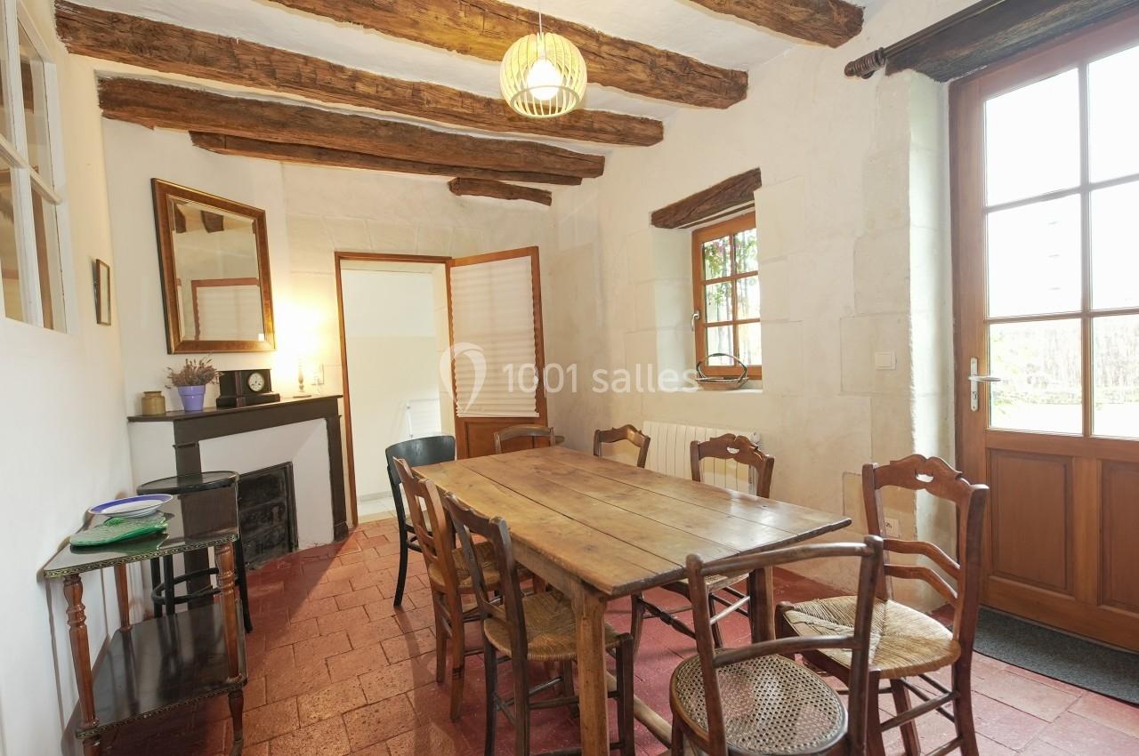 Salle à manger rustique avec table en bois, chaises assorties, poutres apparentes et lumière naturelle.