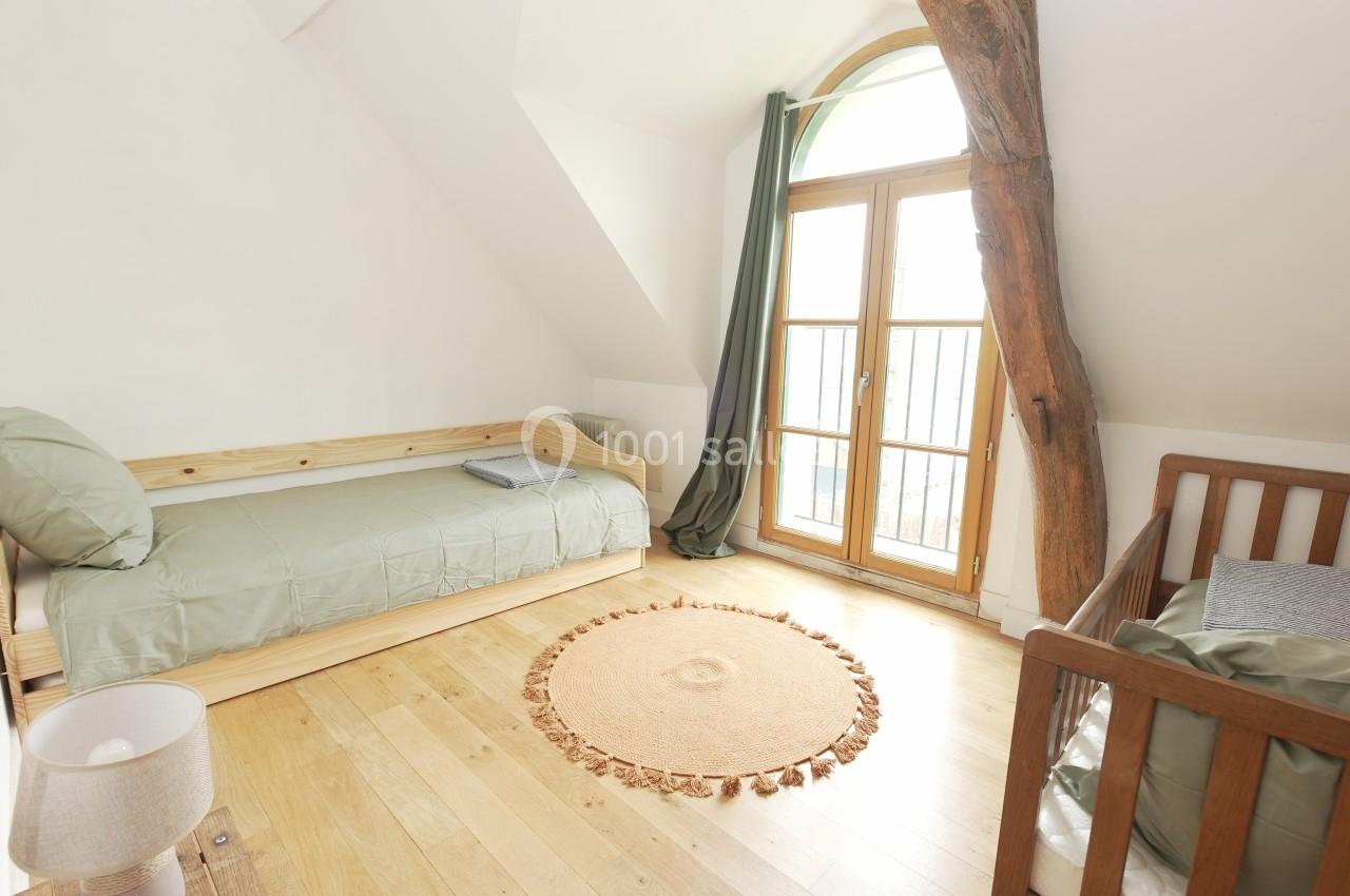 Chambre lumineuse avec lit simple, lit bébé, parquet en bois clair et grande fenêtre avec rideaux verts.