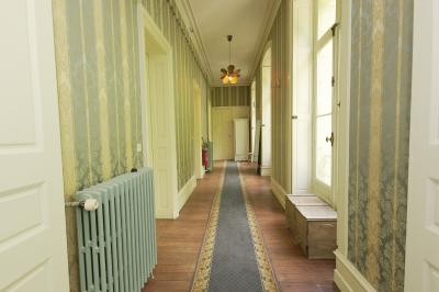 Canapé en velours brun devant une grande fenêtre lumineuse, entouré de rideaux beiges et de meubles en bois.