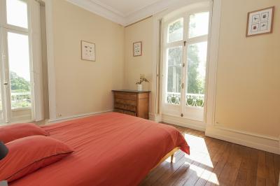 Canapé en velours brun devant une grande fenêtre lumineuse, entouré de rideaux beiges et de meubles en bois.