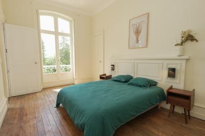 Canapé en velours brun devant une grande fenêtre lumineuse, entouré de rideaux beiges et de meubles en bois.