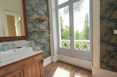 Canapé en velours brun devant une grande fenêtre lumineuse, entouré de rideaux beiges et de meubles en bois.